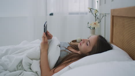 Woman-holding-mobile-phone-while-lying-in-bed-at-home.
